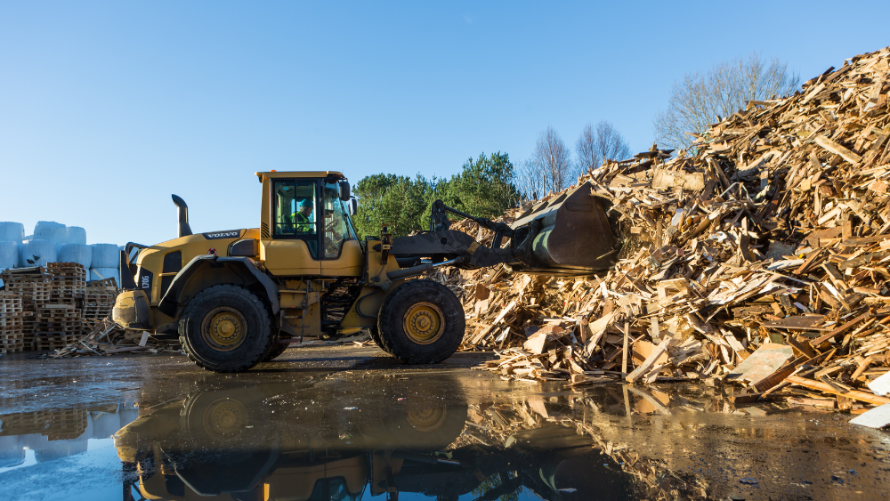 Hjullaster fra Norsk Gjenvinning håndterer store mengder brukt trevirke på et utendørs sorteringsanlegg.