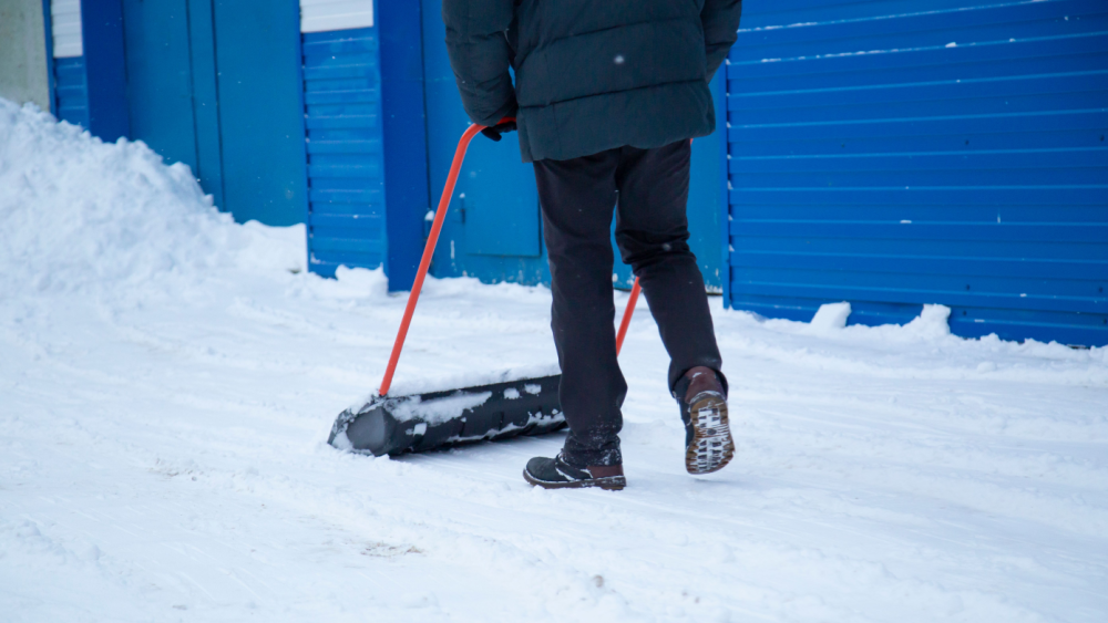 Person fjerner snø foran containere med en snømåker for å sikre trygg avfallshåndtering om vinteren.