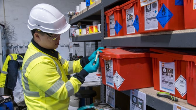 Ansatt håndterer kasse med farlig avfall på mottak, med tydelig merking og verneutstyr.