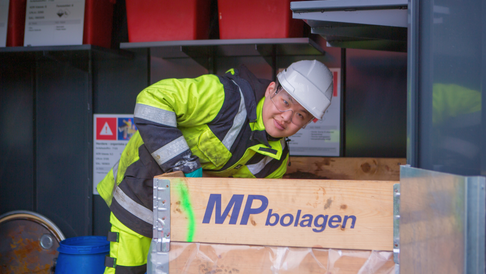 Ansatt merker beholdere med farlig avfall på lager, iført verneutstyr og hjelm.