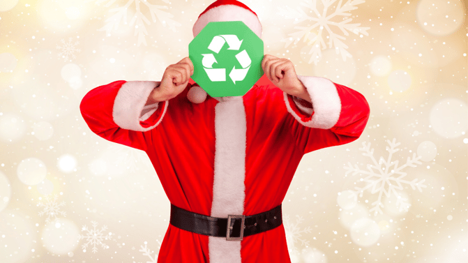 Julenisse som holder et skilt med resirkuleringssymbolet på foran ansiktet