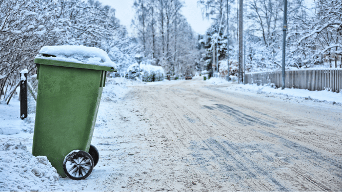 Grønn avfallsbeholder står langs en snødekket, måkt vei. 
