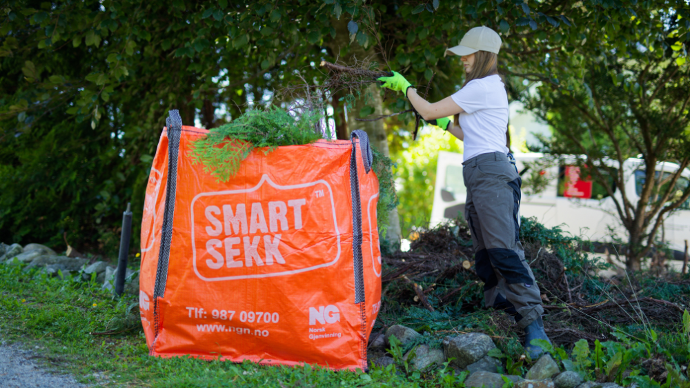 Kvinne rydder hageavfall i en stor oransje avfallssekk merket "SMART SEKK" under dugnad.